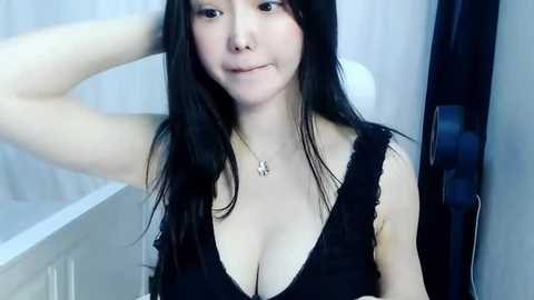 Media: Video of an Asian woman with long black hair, fair skin, and medium-sized breasts, wearing a black lace top, standing in a bathroom with white walls and a shower.