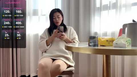 Media: Video of an East Asian woman with long black hair, wearing a white sweater, sitting at a round table with a smartphone, glass, and tissue box in a modern room with white curtains.