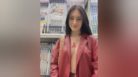 Video of a young woman with long black hair, fair skin, wearing a low-cut red jacket revealing cleavage, standing in a book store filled with shelves of books.