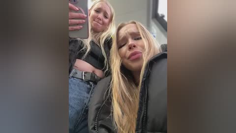 Media: Video of two blonde women in black jackets, one taking a selfie in a bathroom, the other smiling and pouting.