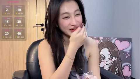 Media: Video of a smiling East Asian woman with long black hair, wearing a sleeveless black top, in a modern room with wooden walls and a calendar.