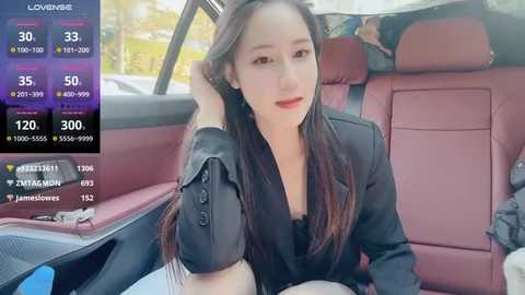 Media: Video of an East Asian woman with long black hair, wearing a black blazer and red lipstick, seated in a car.