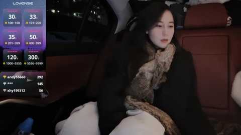 Media: A video shows a young Asian woman with long black hair, wearing a black coat and patterned scarf, sitting in the back seat of a car at night.