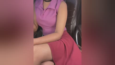 Media: Video of a woman in a purple blouse and red skirt sitting on a black leather chair, her face blurred.