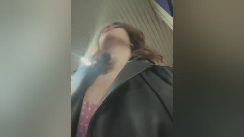 Media: A blurred video of a woman with light skin, wearing a black jacket and a pink lace bra, smoking a cigarette indoors, with a ceiling fan in the background.