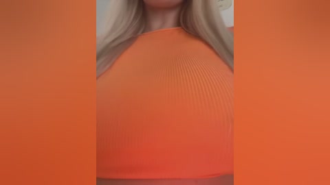 Media: A video of a woman in an orange ribbed crop top, with long blonde hair, partially blurred background, emphasizing the tight fit and texture of the garment.