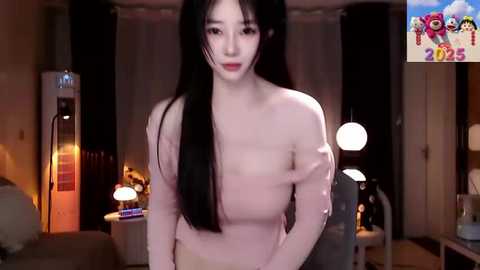 Media: Video of a fair-skinned Asian woman with long black hair, wearing a light pink top, standing in a dimly lit room with modern decor, including a round lamp and a colorful, cartoonish sign in the background.