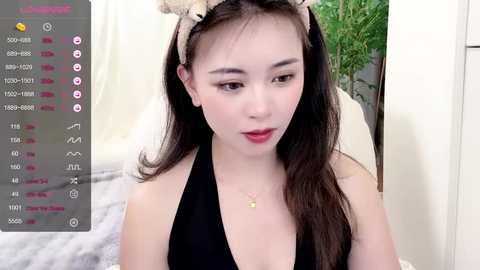 Media: Video of a young Asian woman with long black hair, wearing a black halter top and a cat headband, indoors with blurred background.