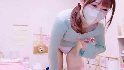 Media: Video of an Asian woman in a pastel room, wearing a light blue sweater, white panties, and a face mask. She bends over, revealing her buttocks.