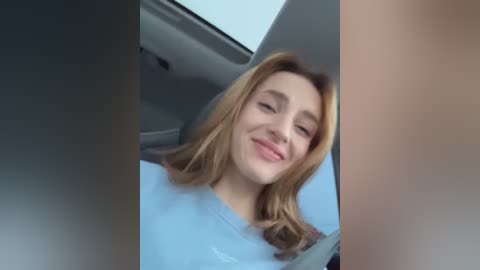 Media: A video of a young Caucasian woman with shoulder-length, light brown hair, smiling, wearing a light blue shirt, sitting in a car with a sunroof.