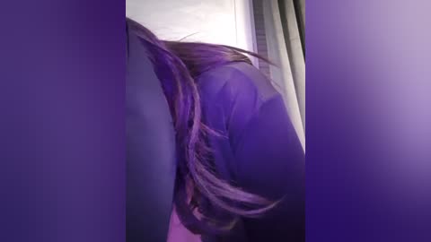 Media: A close-up video of a person's shoulder and back, focusing on a long, wavy, light purple hair tied in a low ponytail. The background features soft, purple curtains and a light-colored wall, creating a serene, intimate atmosphere.