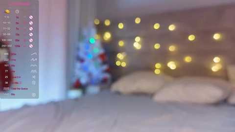 Media: Video of a cozy bedroom with a soft-focus background, featuring a Christmas tree with colorful lights, warm yellow string lights, and a bed with white pillows.