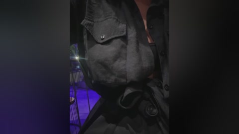 Media: A close-up video of a person wearing a dark, rugged, military-style jacket with multiple pockets and a black belt. The background is dimly lit with purple and blue lights, creating a moody, cinematic atmosphere.