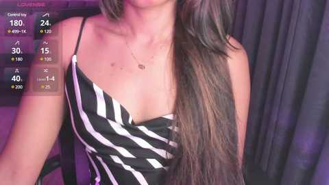 Video of a woman with long brown hair wearing a black and white striped tank top, taken indoors with dim lighting.