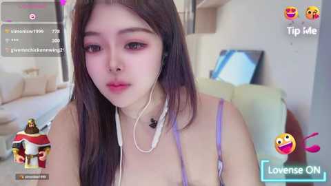 Media: A video of a young East Asian woman with long, straight black hair, wearing a purple spaghetti strap top, listening to music with white earbuds. She is in a modern, minimalist living room with a beige couch.