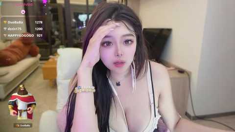 Media: Video of a young East Asian woman with long black hair, wearing a white lace bra, sitting in a modern living room.