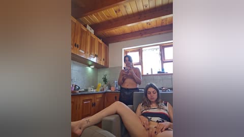 Media: Video of a woman with medium build, dark hair, wearing a striped top, lying on a couch in a rustic wooden kitchen.