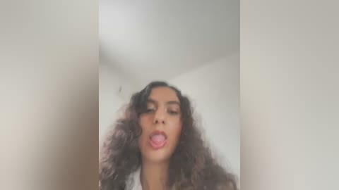 Media: Video of a young woman with curly, shoulder-length hair and medium brown skin, sticking out her tongue against a plain white background.