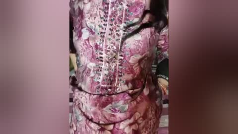 Media: Video of a person wearing a floral-patterned, pink and purple dress with a lace-up bodice, standing indoors with a blurred background.