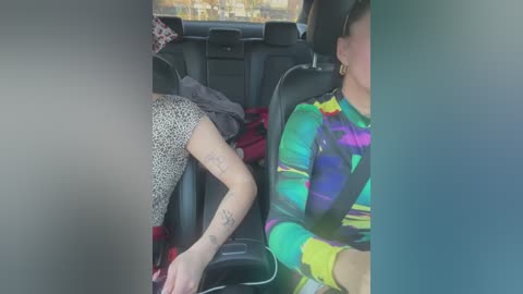 Media: Video of a woman in a colorful, multicolored striped shirt and leopard-print pants sleeping in a car seat, with a blurry background showing the car's interior and a red jacket.