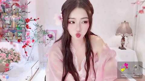 Media: Video of an Asian woman with long brown hair, wearing a pink robe, blowing a kiss. Background includes a lamp, flowers, and digital social media interface with likes and comments.