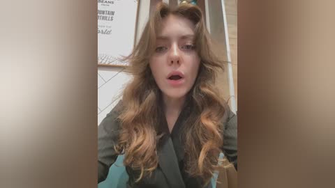 Media: A video of a young Caucasian woman with long, wavy brown hair, wearing a teal robe, looking surprised or shocked, with a tiled bathroom background.