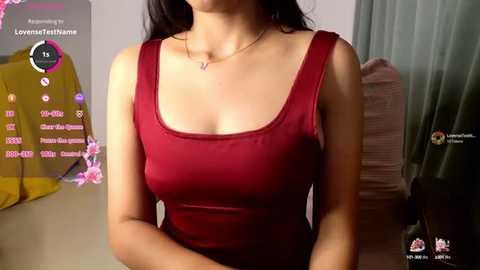 Media: Video of a young woman with long black hair, wearing a red sleeveless top, in a bedroom with a yellow dress and green curtains in the background.