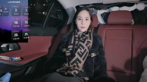 Media: Video of a young woman with light skin, dark hair, and a patterned scarf, sitting in the back seat of a red car, looking out the window at night.