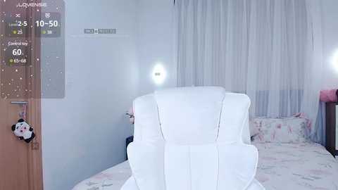 Media: A video of a modern, minimalist bedroom with white decor, including a plush white armchair, a white bed with pastel floral sheets, and sheer white curtains. A door with a panda keychain is visible in the left corner.