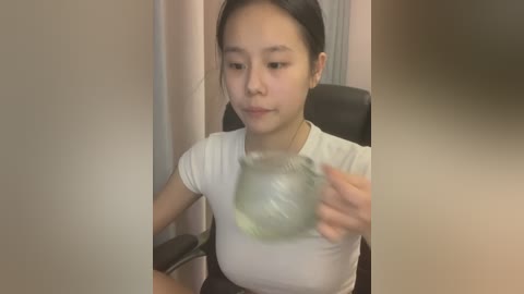 Media: A video of an East Asian woman with straight black hair, wearing a white t-shirt, sitting in an office chair. She is holding a clear plastic bag filled with air, creating a bubble effect.