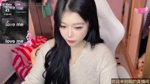 Media: Video of an Asian woman with long black hair, fair skin, wearing a beige ribbed sweater, sitting on a white chair in a pink room. Text overlays read, \"love me.\