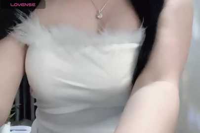 Media: A video of an Asian woman with fair skin, wearing a tight white top with fluffy white feather shoulders. She has long black hair and a delicate necklace.