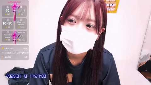 Media: Video of a young Asian woman with long, straight brown hair wearing a white surgical mask, a dark jacket, and a blue shirt, indoors, with a digital clock and health bar overlay.