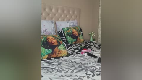 Media: Video of a bedroom with a beige tufted headboard, a green bedspread with a patterned pillow featuring a woman with a headscarf, and a white duvet with black leaf design.