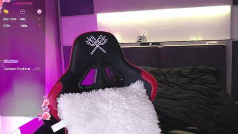 Media: Video of a gamer's chair with a red and black design, featuring a white fur throw over the backrest, in a modern, dimly lit bedroom with purple accents and a bed with dark bedding.