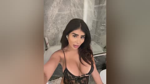 Media: A video of a Latina woman with long dark hair, wearing black lace lingerie, standing in a marble-tiled bathroom, taking a selfie.