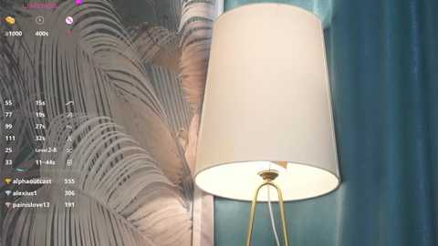 Media: Video of a teal wall with a white lampshade and a lush, leafy wallpaper in the background. The lamp has a golden stand.