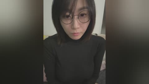 Media: A video of a young Asian woman with straight black hair and glasses, wearing a black turtleneck, sitting indoors against a blurred background.