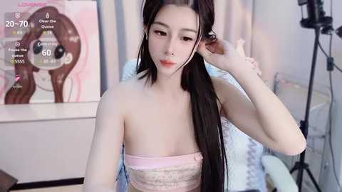 Media: Video of an East Asian woman with long black hair, fair skin, and a slender physique, wearing a pink strapless top, adjusting her hair in a room with soft lighting and a white wall.