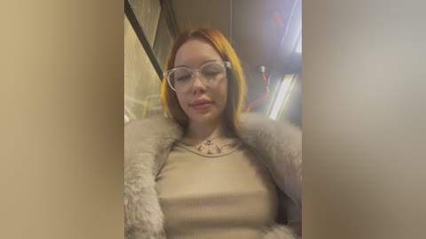 Media: Video of a fair-skinned woman with red hair, wearing large glasses, a beige top, and a fur-trimmed jacket, sitting in a subway car.