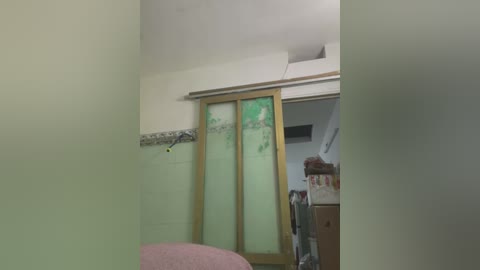 Media: A video of a small, unfinished bedroom with white walls and a half-built wooden closet door. The room features a pink armchair, a mess of clothes, and a partially visible bed in the background.