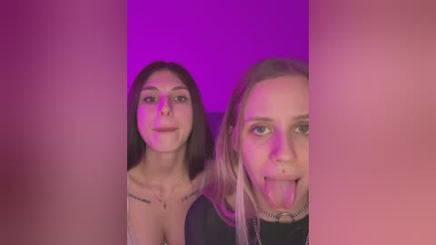 Media: Video of two young women with long hair, one with a nose ring, both sticking out their tongues, under purple lighting, creating a playful, slightly provocative atmosphere.