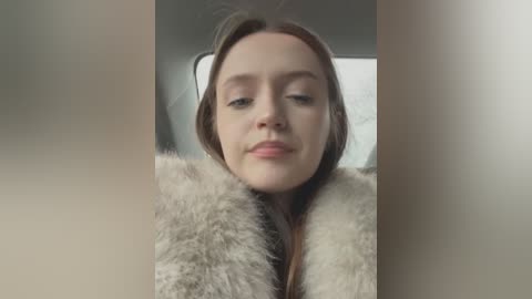 Media: A video of a young woman with fair skin and light brown hair, wearing a beige fur coat, with a neutral expression.