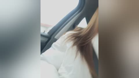 Media: A blurred video of a person's head and shoulder in a car, with long brown hair, wearing a white shirt. The background shows the car interior and window.