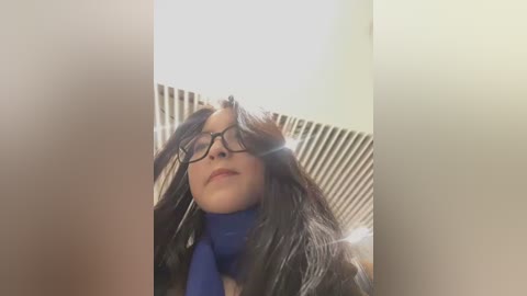 Media: A video of a young woman with long dark hair, glasses, and a blue scarf, standing in front of a radiator in a dimly lit room.