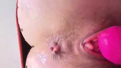 Video of a close-up of a woman's vulva with a pink vibrator inserted, showing labia and clitoris, with visible skin texture and natural lighting.