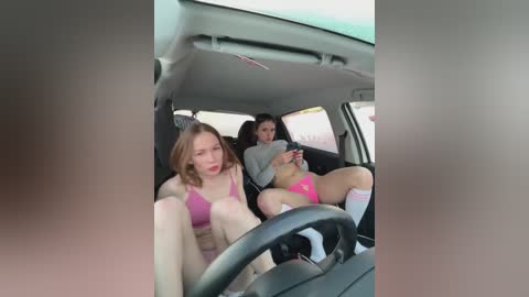 Media: A video captures two women in a car, both wearing pink underwear and knee-high socks. They are sitting in the backseat, one with a pink bra and the other in a gray top.