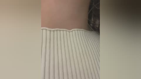 A close-up video of a person's bare skin and the hem of a beige ribbed sweater, with a blurred background, capturing a casual, everyday moment.