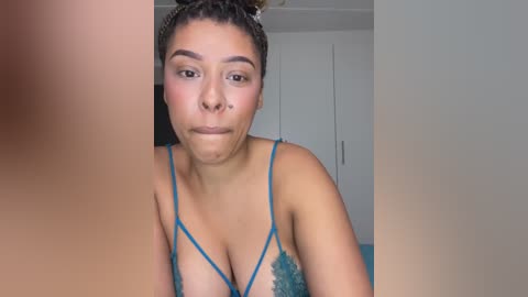 Media: Video of a young, light-skinned woman with braided hair, wearing teal lace lingerie, making a pouty face; background shows a white door and part of a bed.