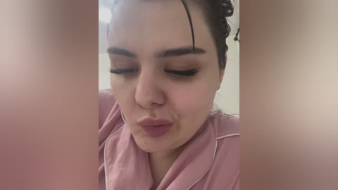 Media: Video of a young woman with light skin, dark hair, and closed eyes, puckering her lips in a kiss, wearing a pink robe.